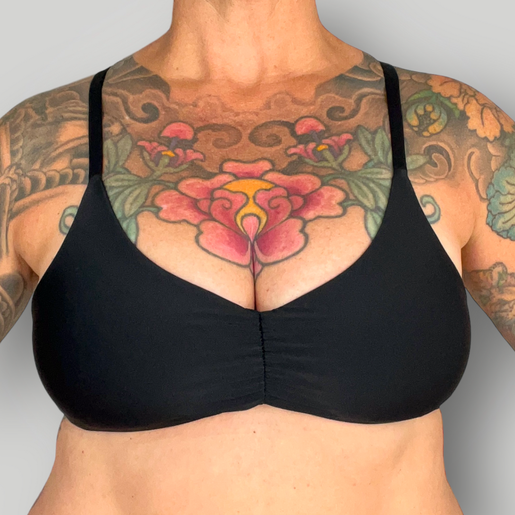 Black bikini top worn by a person with tattoos on a gray background