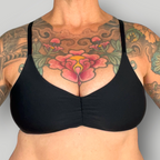 Black bikini top worn by a person with tattoos on a gray background